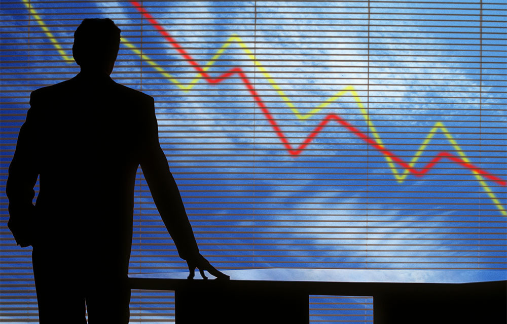 Silhouette of a businessman turned away looking at enlarged, downward trend lines.