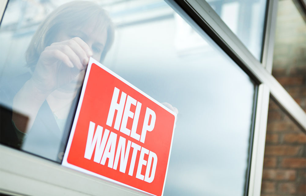 A business owner putting up a help wanted sign on their storefront window.