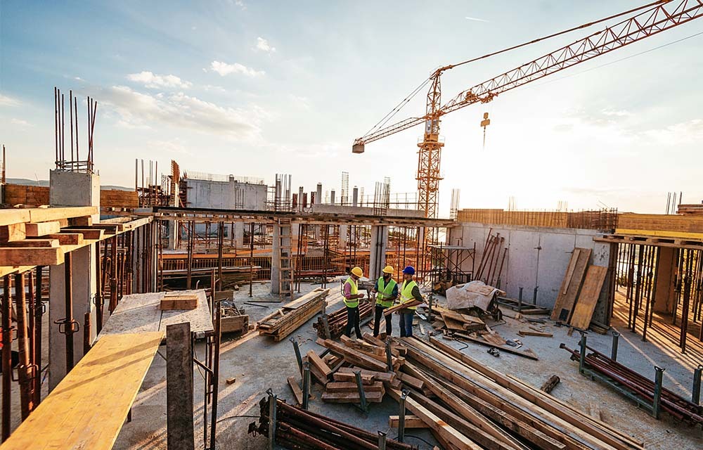 Three construction workers discussing their plan, surrounded by building materials, scaffolds, and a crane.